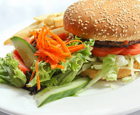 Image of burger in a bun with tomato and a side salad with a few chips. 