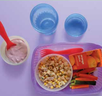 Image of a packed lunch with a bowl of tuna and sweetcorn pasta, a yoghurt pot, vegetable sticks and a carton of orange juice. 