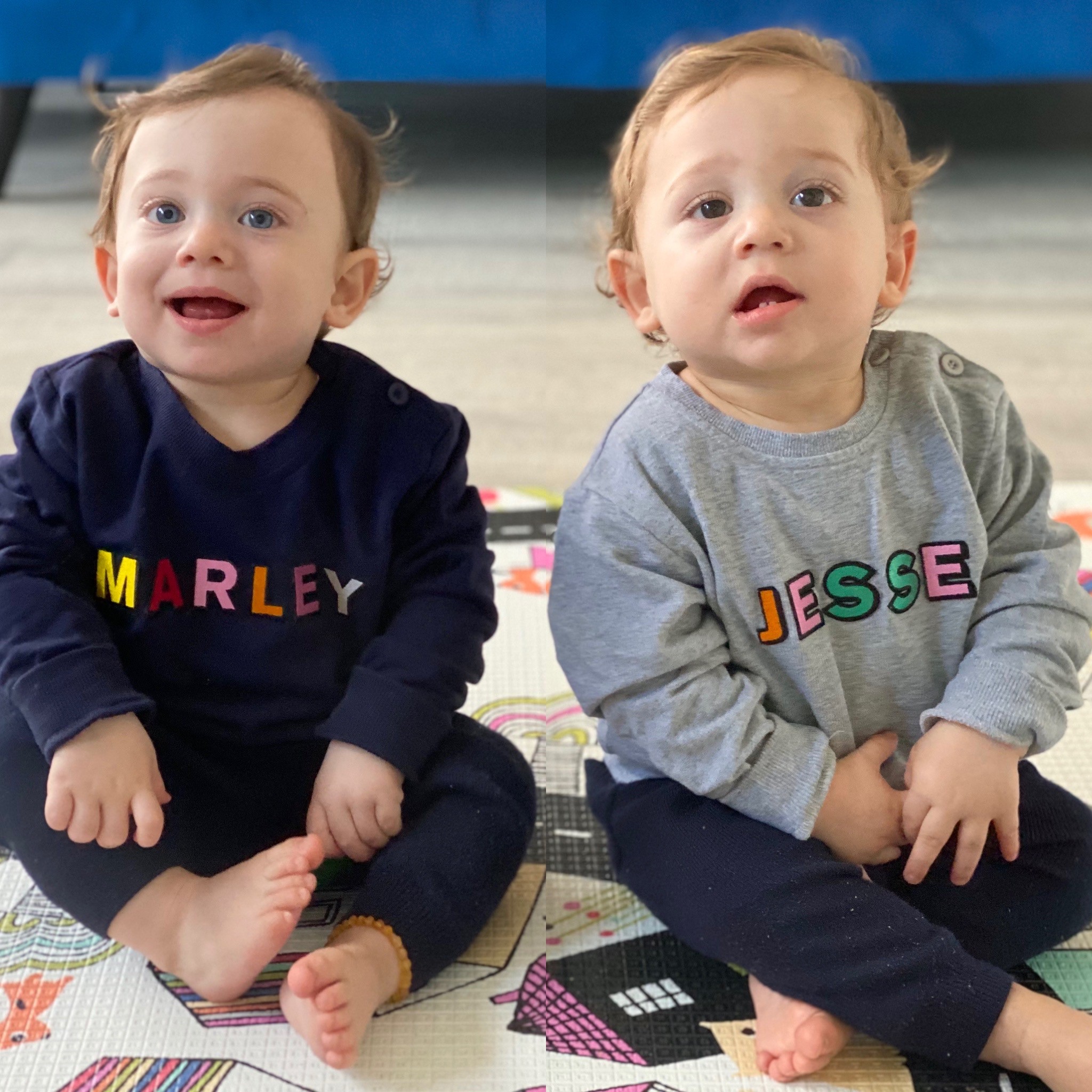 Twin baby brothers modelling custom sweatshirts, one navy and one grey, both with rainbow coloured letters spelling their names