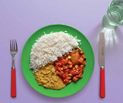 Vegetable curry and lentil dahl on a plate with rice. There is glass of water and cutlery on the table. 