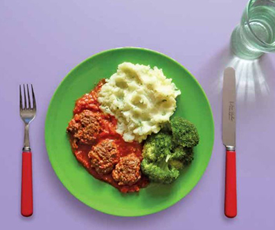 Meatballs on a plate with broccoli and mashed potatoes. There is a glass of water and cutlery on the table. 