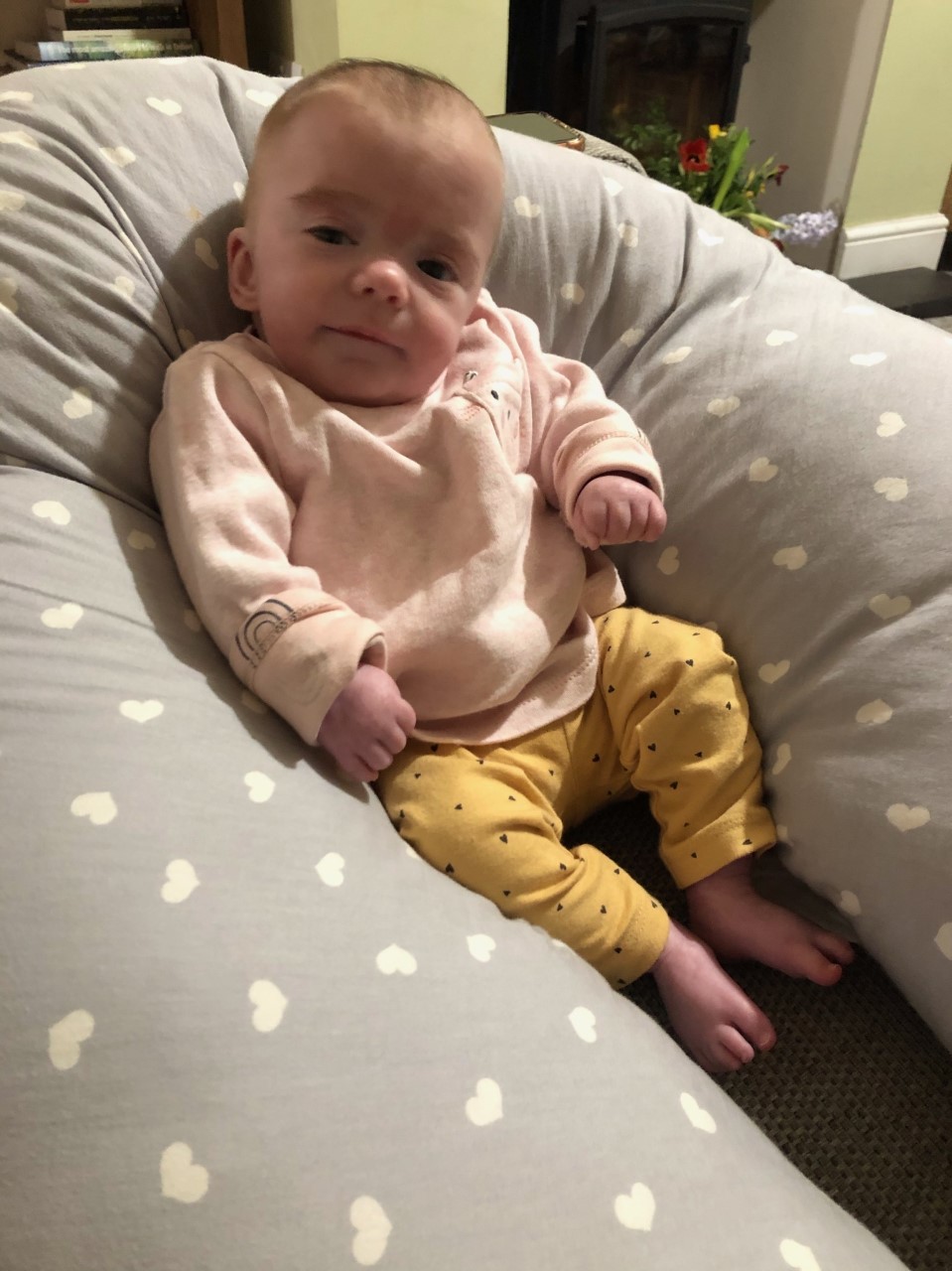 A baby girl sitting propped up against a spotty ringed nursing cushion