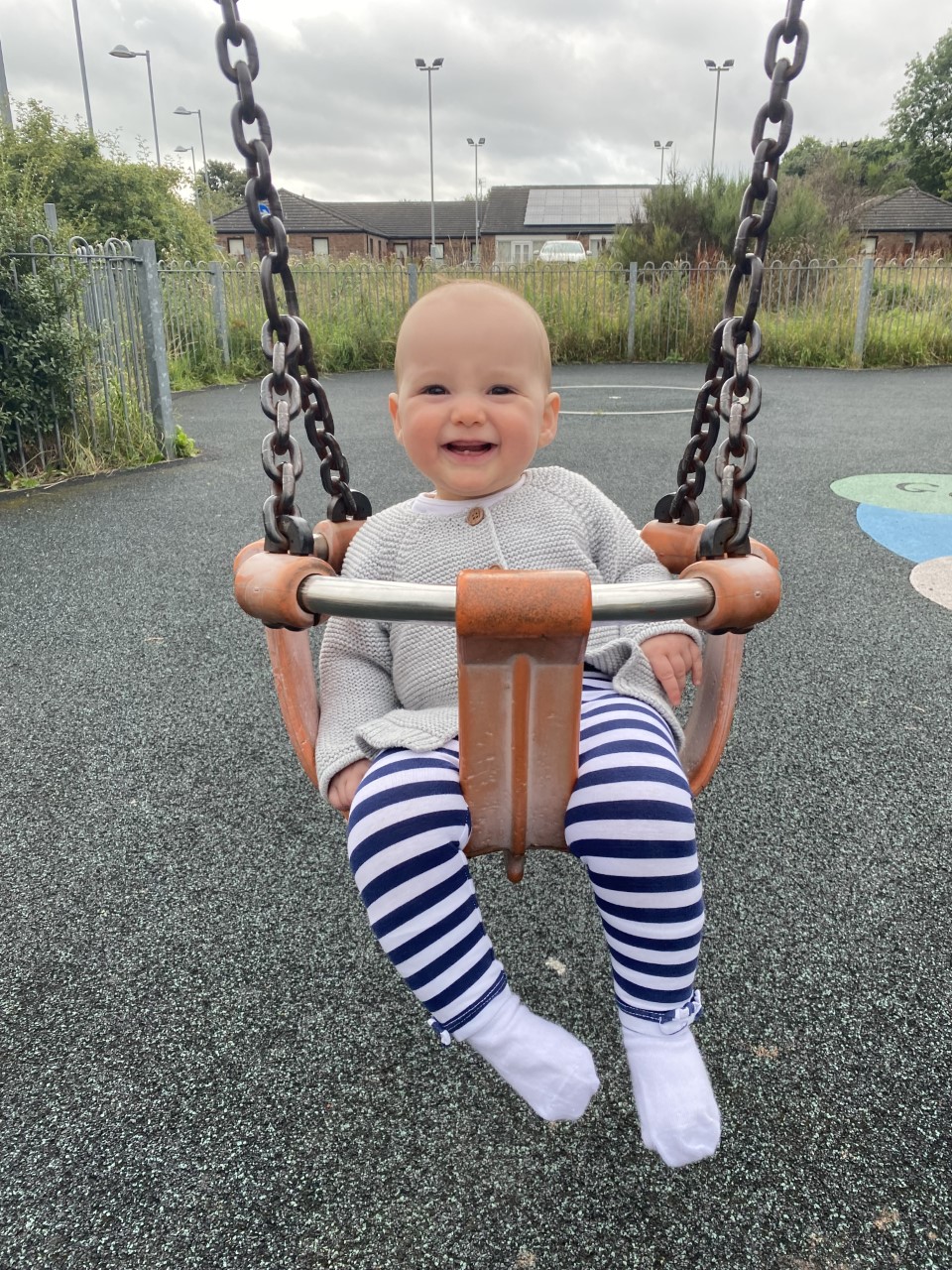 A baby girl on a swing in an outdoor play area