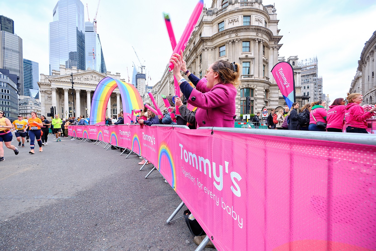 Pink Tommy's banners along a safety banner and lots of Tommy's staff cheering runners on
