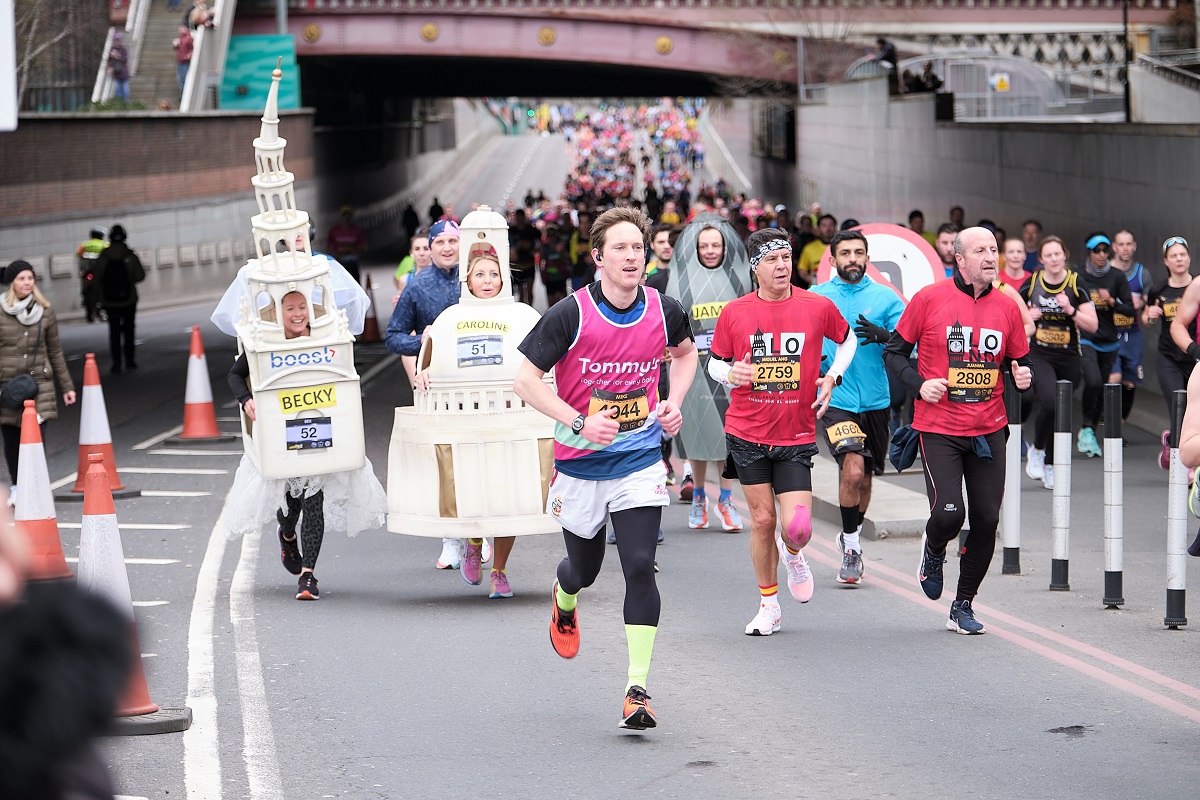 A group of runners pass under a bridge, several dressed in large costumes depicting London landmarks
