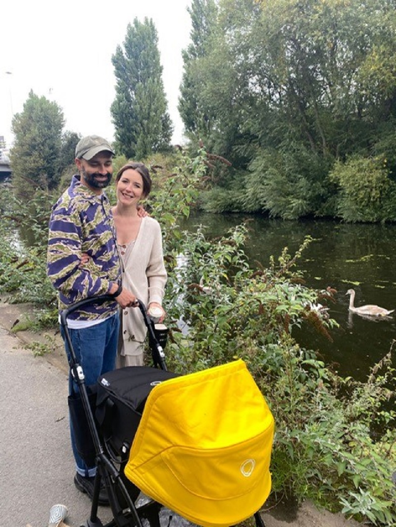 Jess and her partner stand on a canal path with baby Nyla in a yellow pram